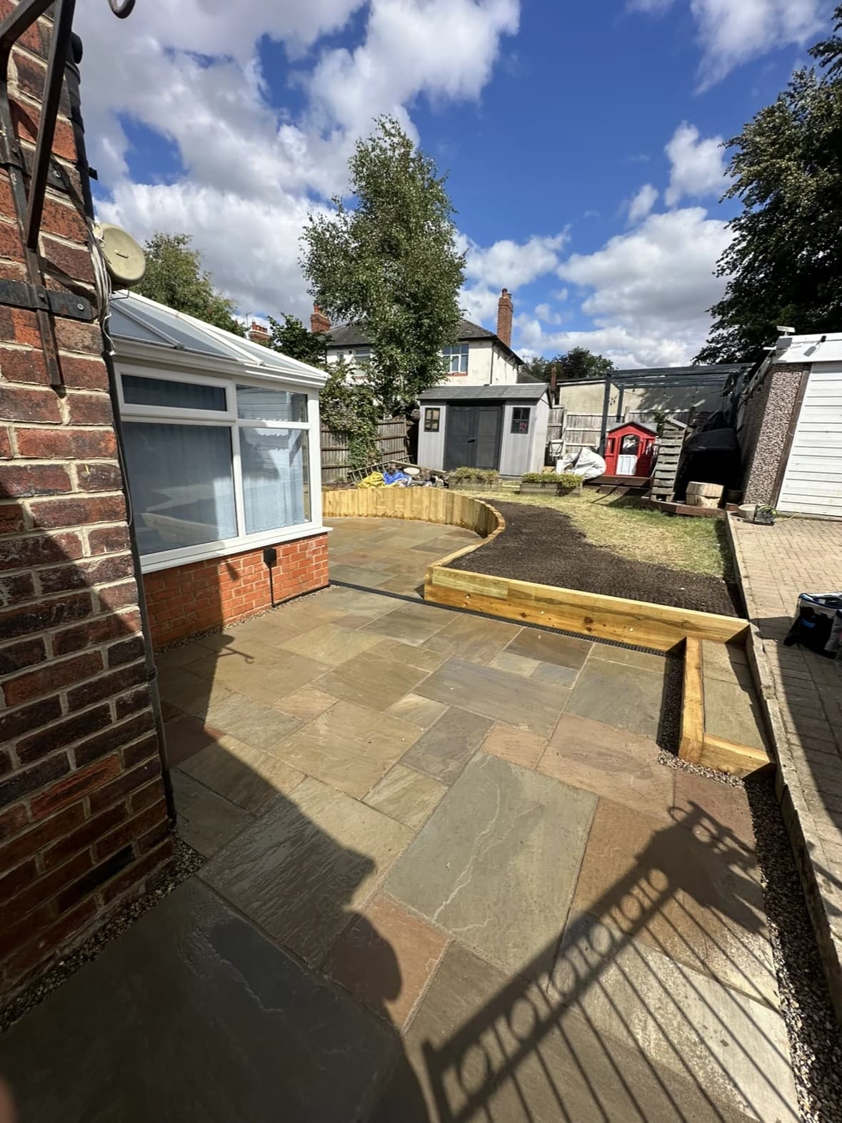 Stone patio beside a conservatory with curved timber edging leading into the garden