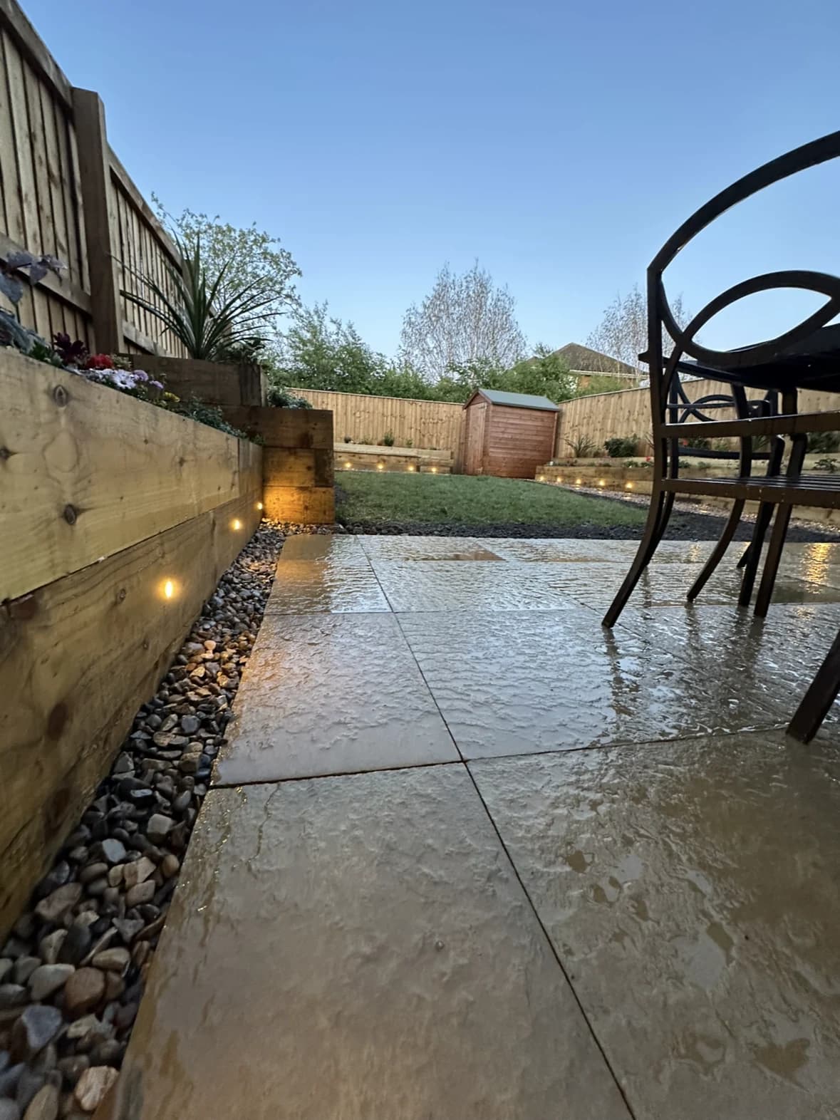 Garden patio beside a timber raised bed with inset lighting and a pebble border